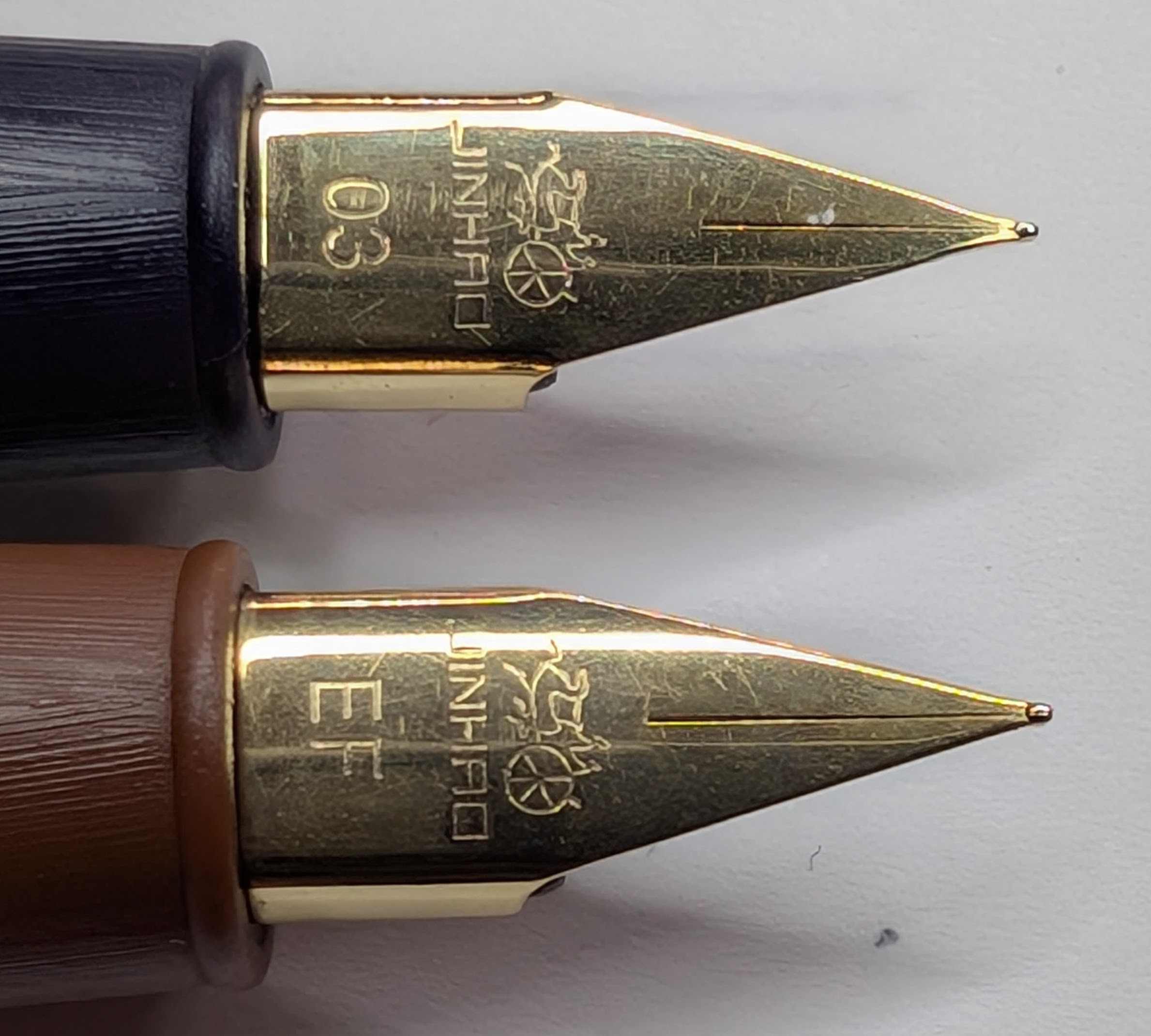 Photo of two fountain pen nibs taken from the top-down. Both nibs are labeled with "Jinhao" and the company logo. The top nib is marked "03", the bottom nib is marked "EF". The tip of the nib on the top pen is ever so slightly thinner.