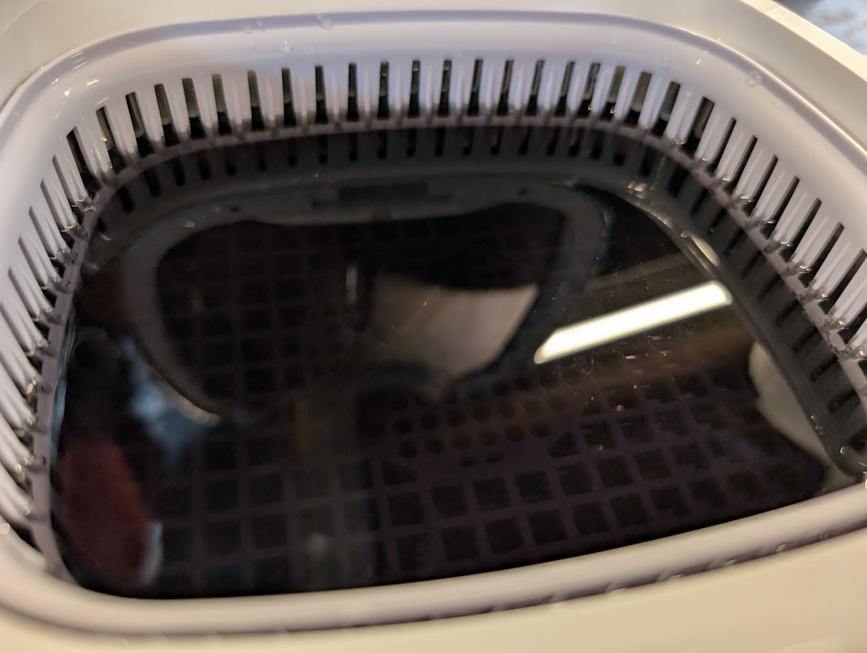 Photo of an ultrasonic cleaner. The inside is filled with a murky, dark black-ish fluid. Barely visible inside is a fountain pen nib.