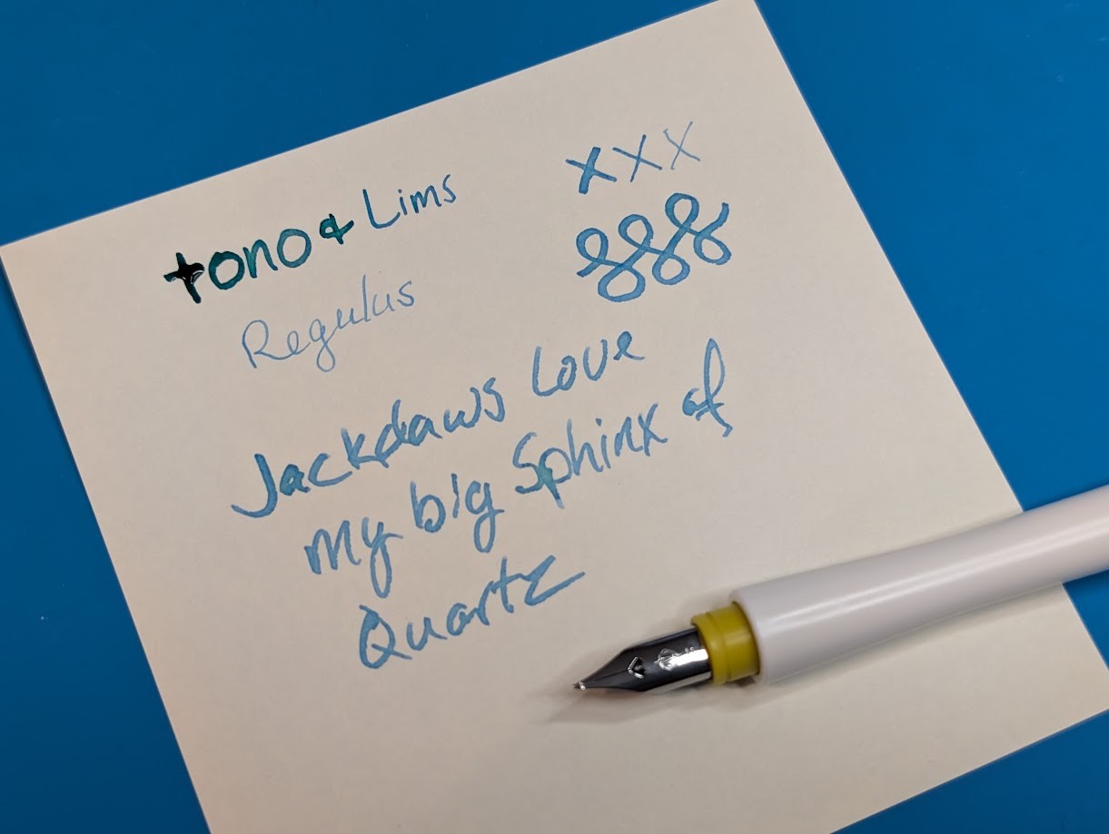 Photo of a writing sample on paper written with the Fude nib in various heights. It starts with "Tono &" written at max width, "Lims" written at minimum width, and "Regulus" written with the nib reversed (upside-down). Followed by three "X" written in each of those widths. Then three curlicues at max width. Under that is "Jackdaws love my big sphinx of quartz" written with some line variation.