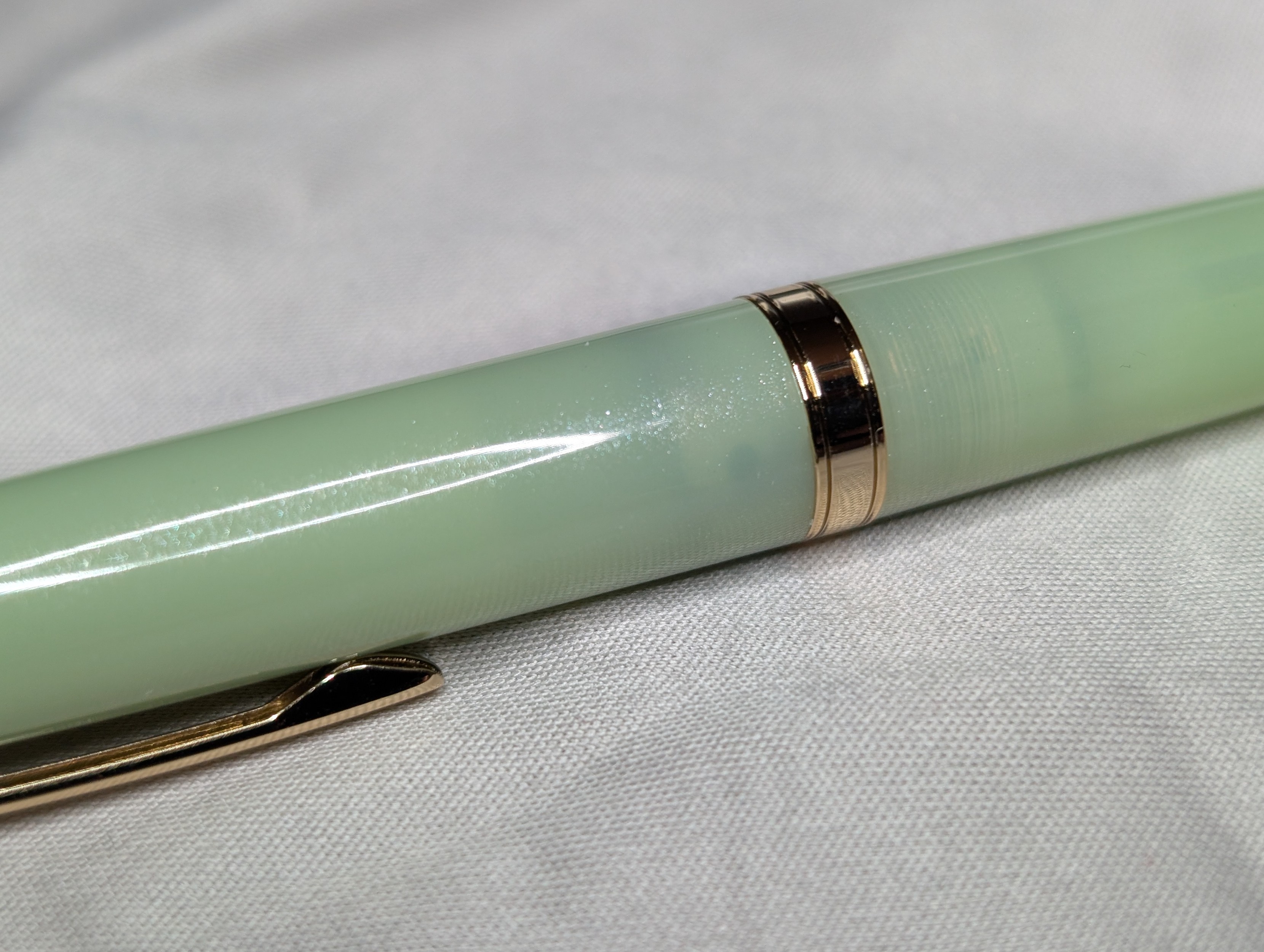 Photo of a light green fountain pen body. Small bits of shimmer particles catch light and sparkle, but they minimal and are only visible in a narrow band down the center.