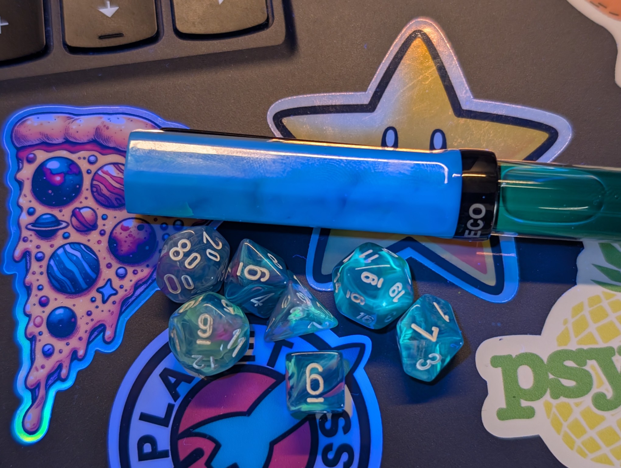 Same as the previous photo but under UV light. The green parts of the dice are glowing brightly. The pen cap is glowing blue. The ink in the pen is dimly glowing green.