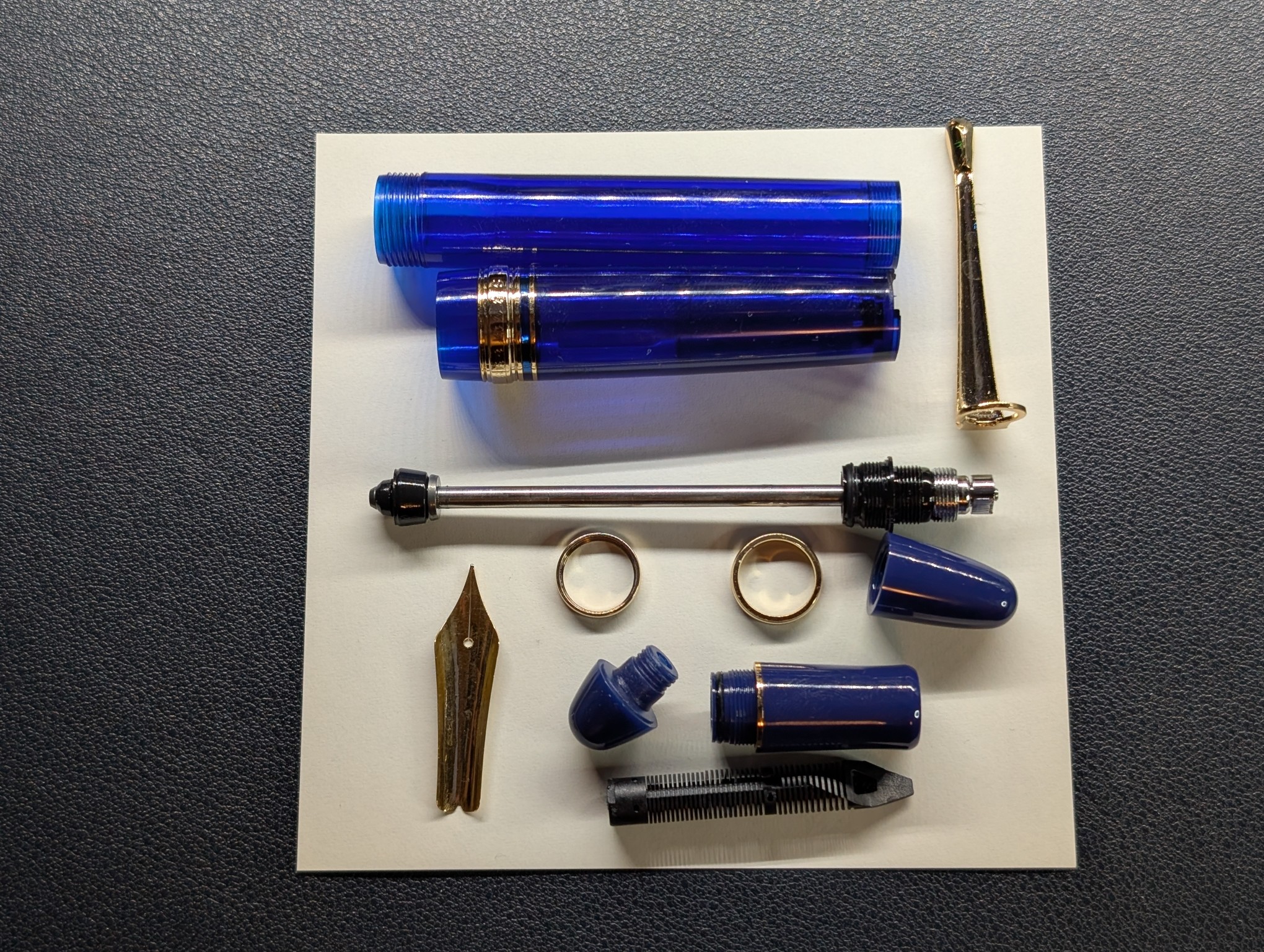 Photo of a disassembled vacuum filler fountain pen on a piece of paper. The pieces are arranged in a haphazard manner.