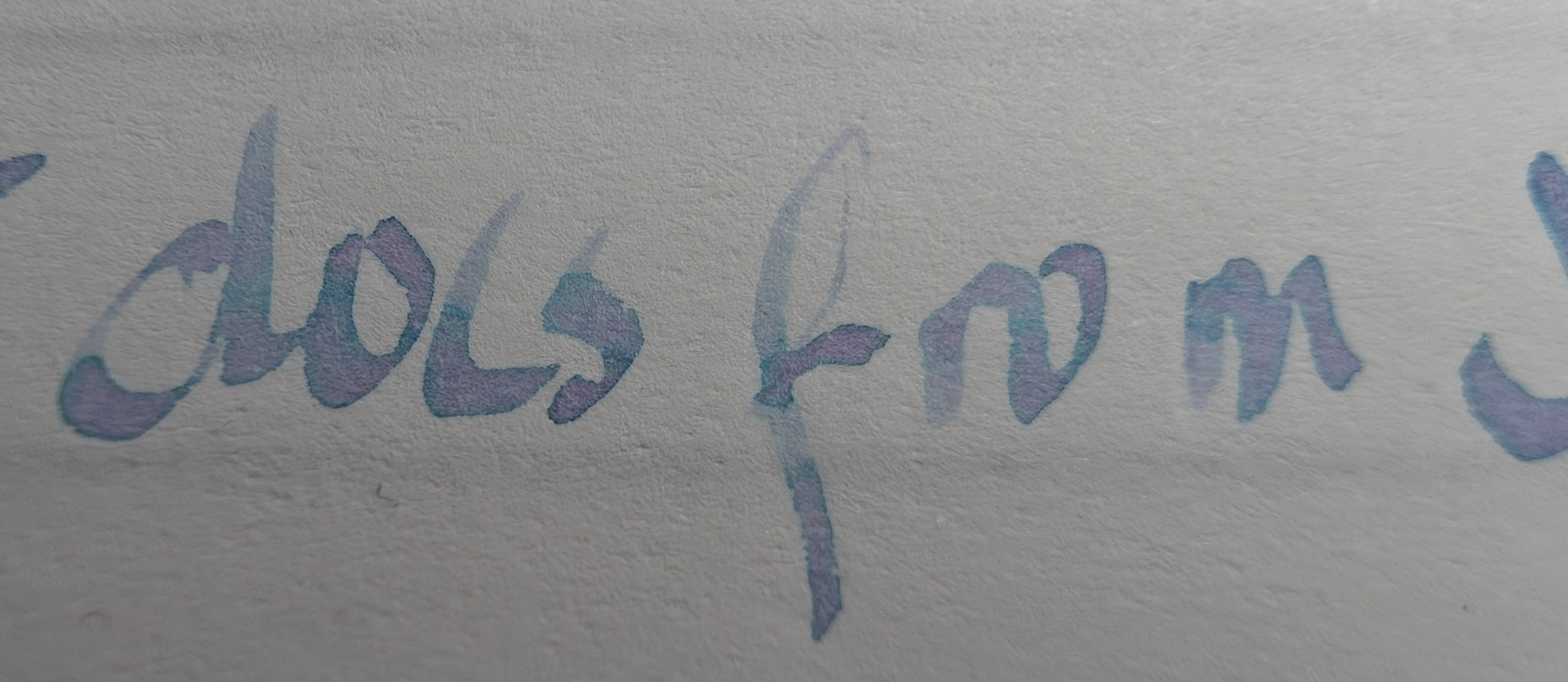 Photo of writing on paper, close-up of a partial sentence "docs from J" The ink is mostly a pale slate blue but in areas with more ink it shades to more pinkish