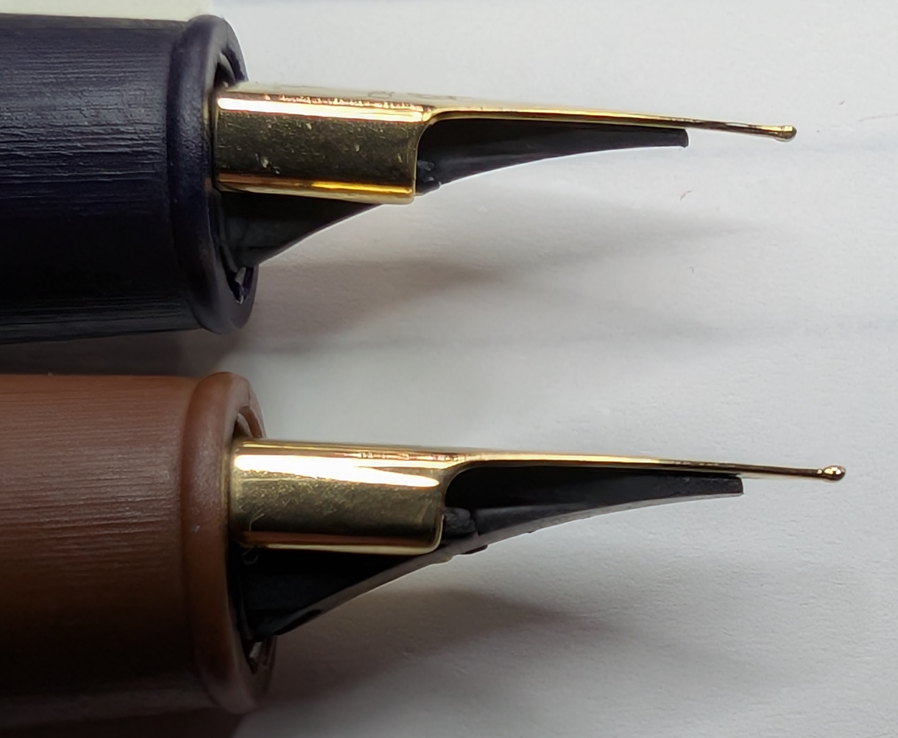 Photo of two fountain pen nibs taken from the side. The tip of the nib on the top pen is has a little more material on the underside, the bottom pen has more on the upper side.