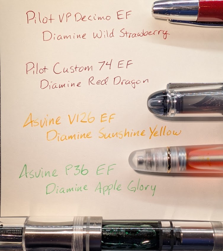Photo of four writing samples on paper and partial views of four pens. 1: "Pilot VP Decimo EF / Diamine Wild Strawberry" in bright red ink, the tip of a red capless fountain pen with a silver tip is slightly visible. 2: "Pilot Custom 74 EF / Diamine Red Dragon" in dark red ink, the tip of a clear capped fountain pen is slightly visible. 3: "Asvine V126 EF / Diamine Sunshine Yellow" in yellow-orange ink. The tail of a clear, but frosted, fountain pen is visible with orange-ish ink inside. 4: "Asvine P36 EF / Diamine Apple Glory" in bright green ink. The middle section of a clear fountain pen is visible, the inside is full of green ink.