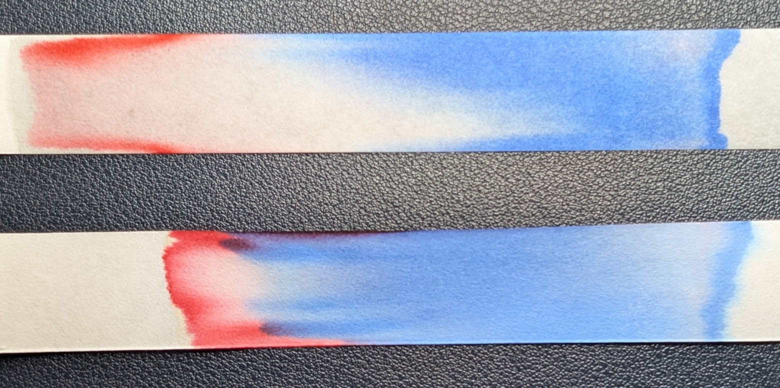 Photo of two strips of chromatography paper. Both are similar, having a light blue on the left, some white area in the middle and finishing with a light red on the left. The lower strip has some purple around the edges and in the transition area between red and blue. The top strip was made using a metal dip pen to draw a line. The bottom strip was made using a the back of a glass dip pen to draw the line.