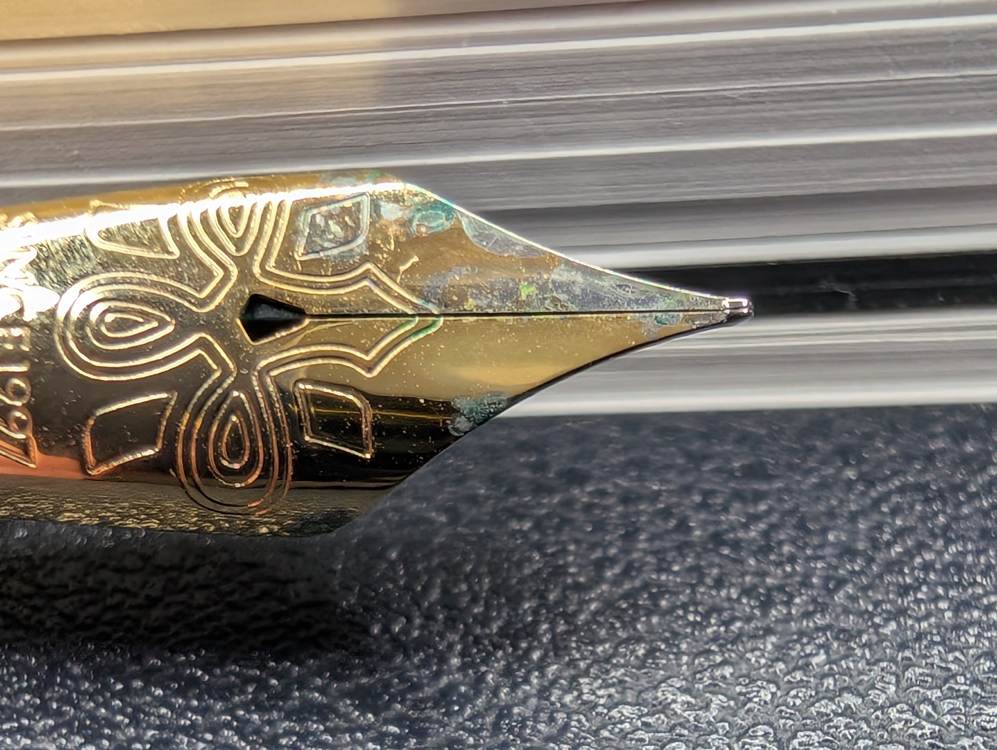 Photo of a fountain pen nib up close. Most of the nib is covered in gold tone plating. The left "tine" of the nib has a lot of bare metal visible. Areas on curve of both sides have lost plating and have exposed metal. A couple more areas are also green in color where the plating is missing.