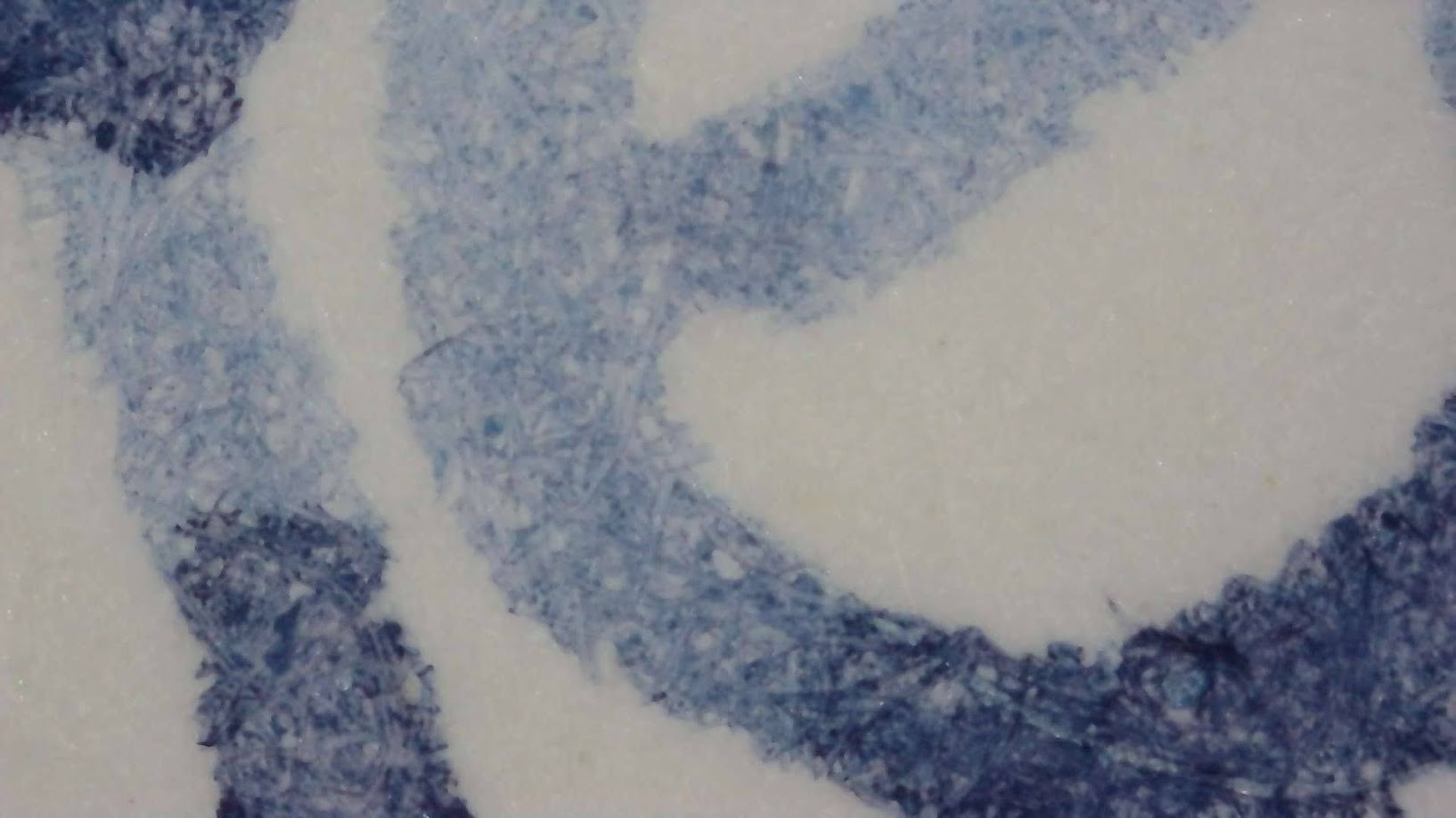 Photo of writing with ink under microscope. Paper fibers are visible, colored by blue-gray ink. Some areas are significantly darker than others where more ink has pooled.