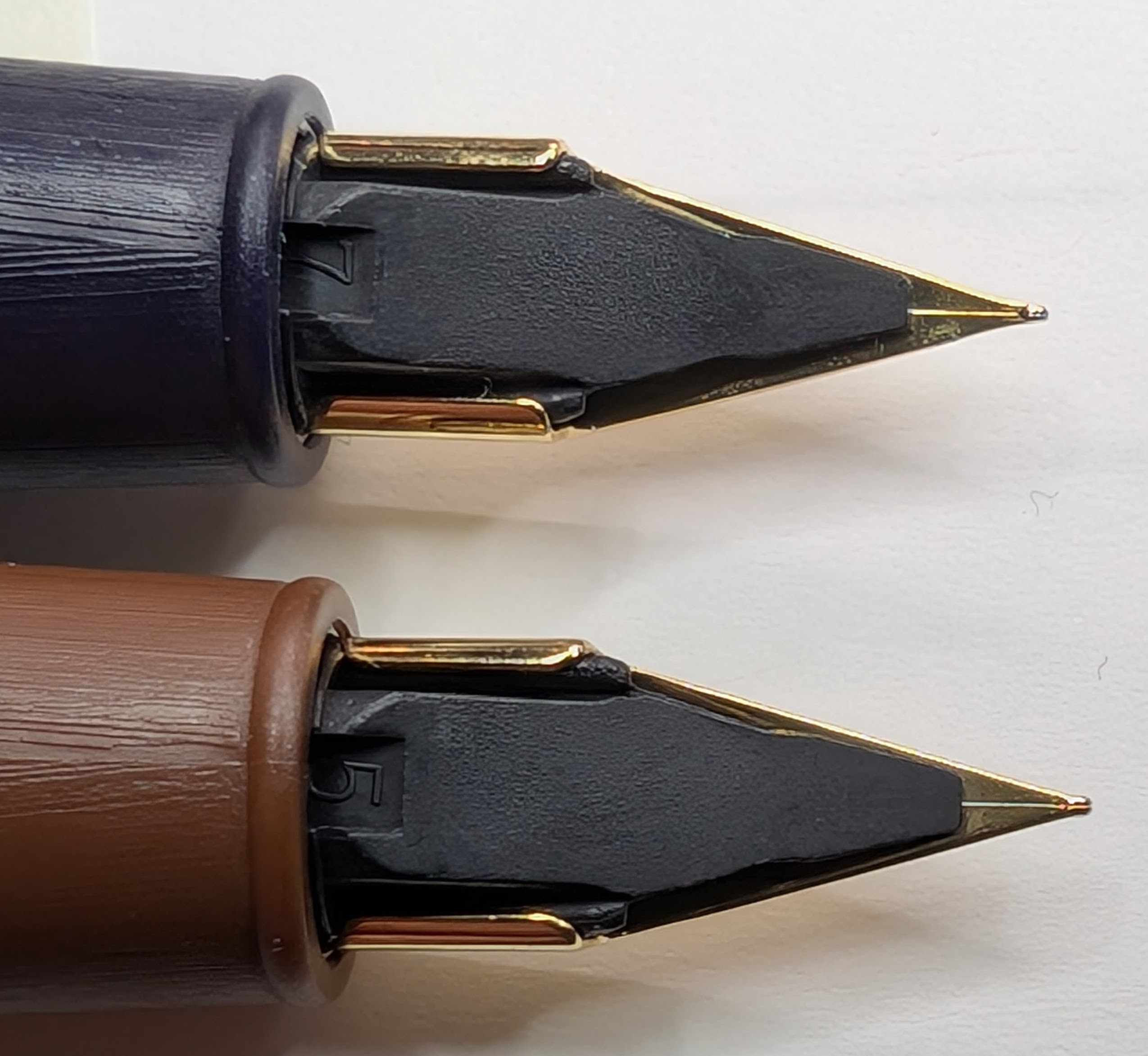 Photo of two fountain pen nibs taken from the bottom. The tip of the nib on the top pen is ever so slightly thinner, shorter, and shinier.