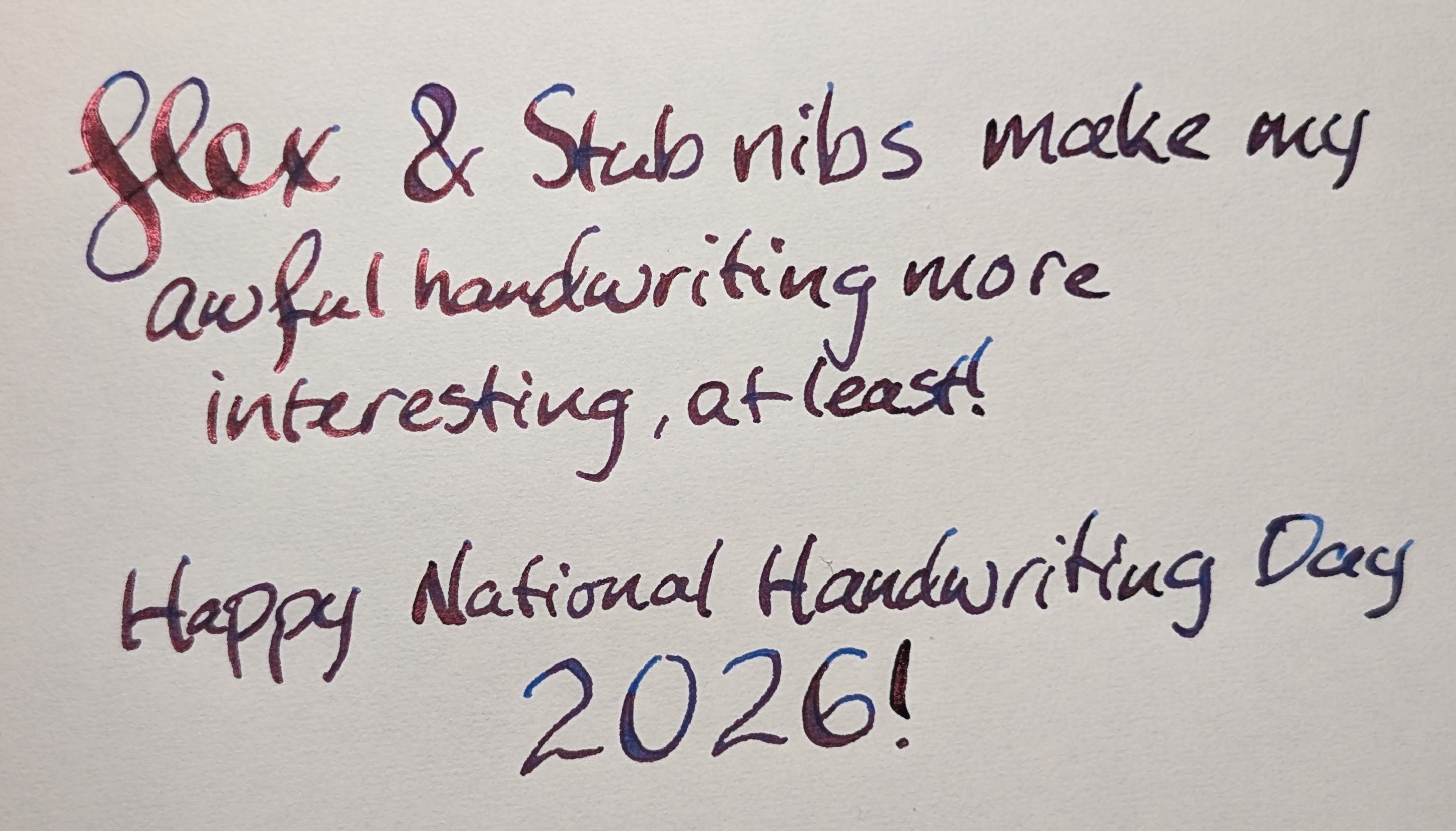 Photo of handwriting on paper reading "Flex & Stub nibs make my awful handwriting more interesting, at least! / Happy National Handwriting Day 2026!" The words are written with a flex nib, some words have a lot of line width variation. The ink is dark blue with red sheen where the light catches it.