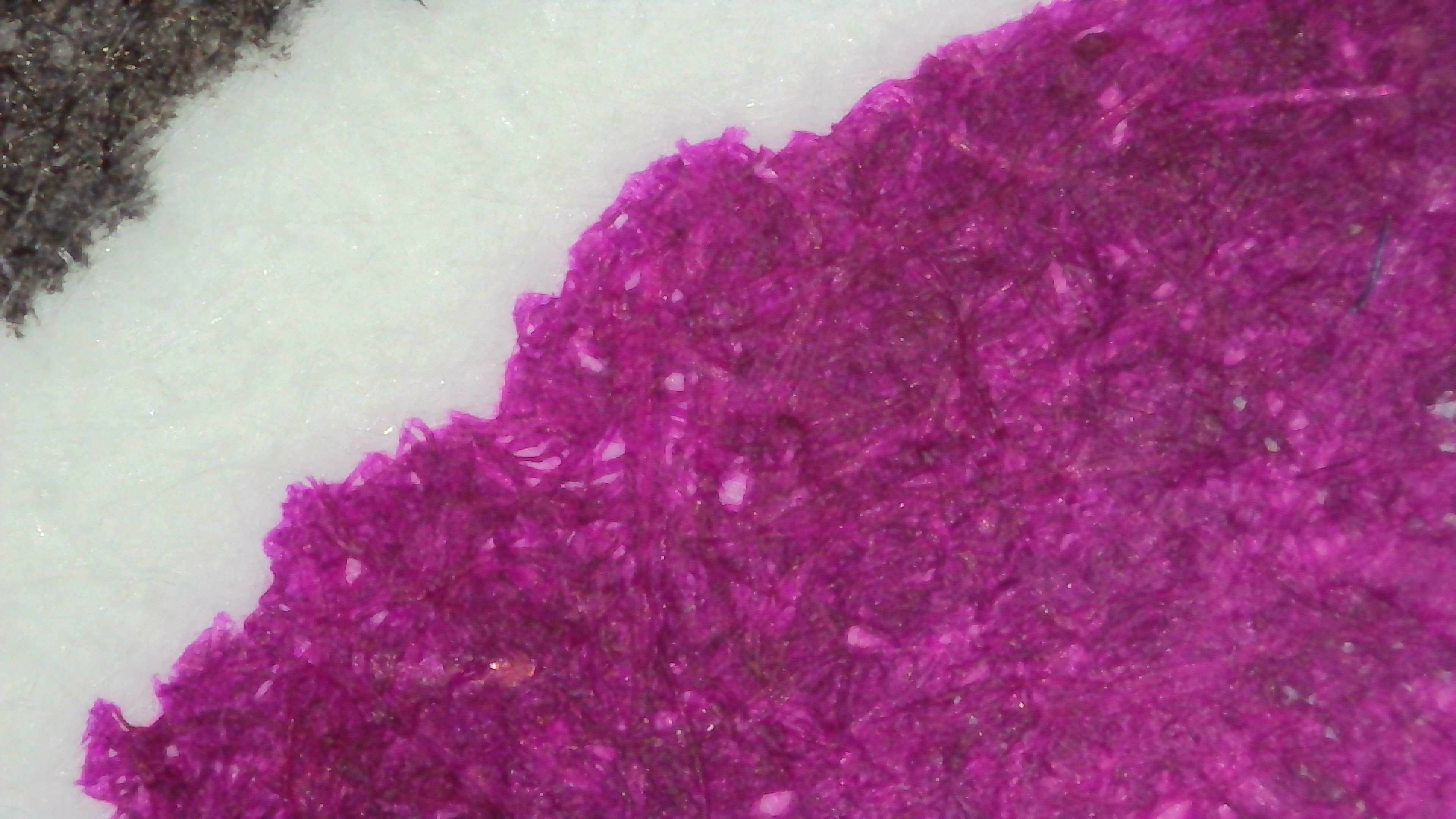 Photo of ink swatch on col-o-ring paper under magnification. The ink looks even dark magenta. Some visible paper fibers are even darker. Color is fairly even, no visible shading or pooling. Line edges are rough and uneven.