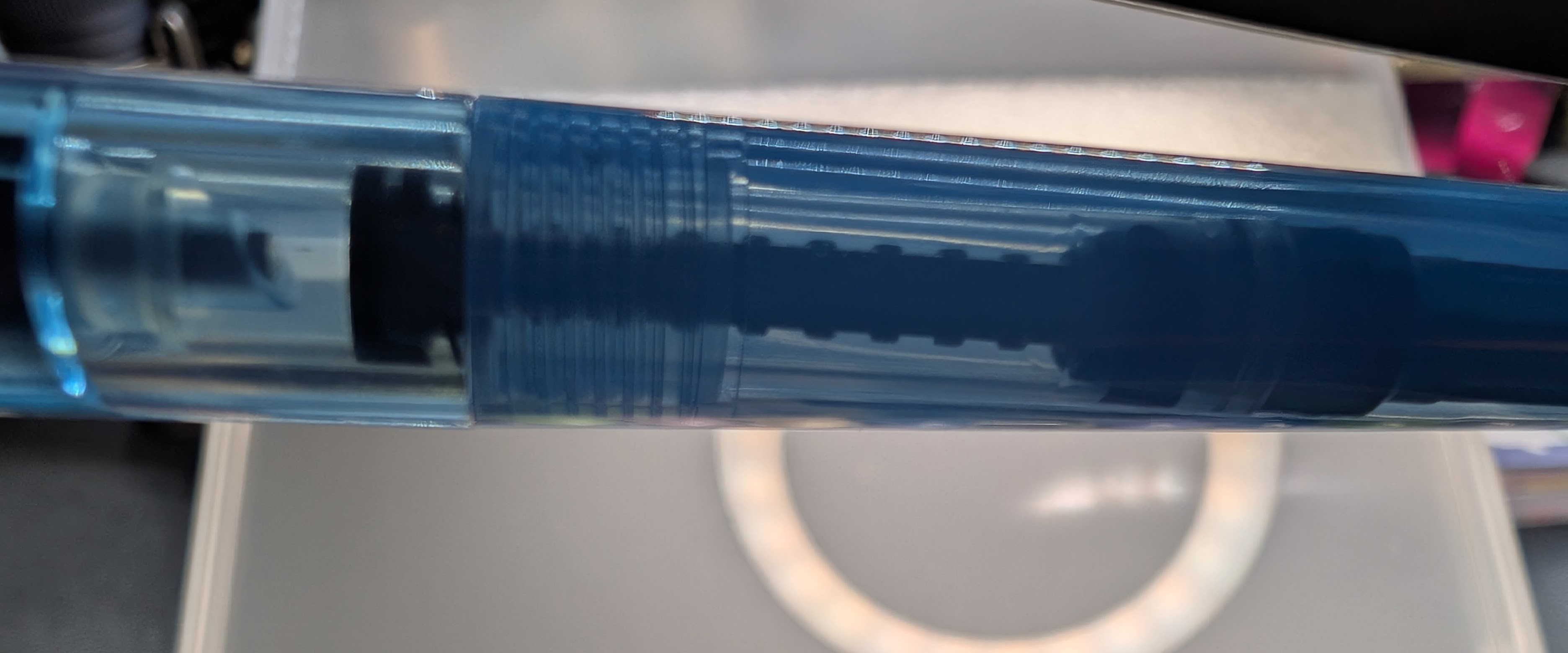 Photo of a translucent plastic fountain pen body and transparent section, both tinted blue. The converter is easily visible through both the section and the body.