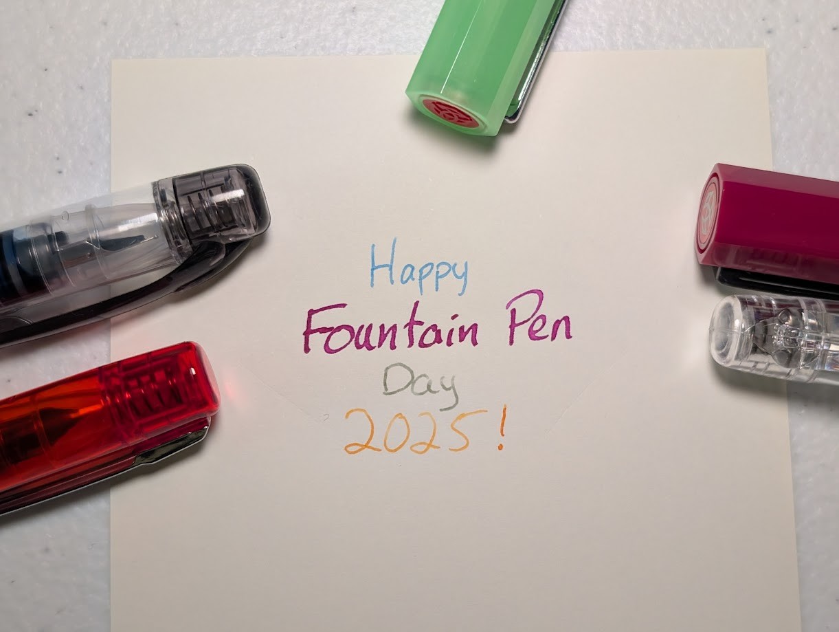 Top-down photo of writing on paper surrounded by the caps of several pens all under natural light. It reads "Happy Fountain Pen Day 2025!" "Happy" is written in blue ink. "Fountain Pen" is written in fuchsia ink "Day" is written in olive green ink "2025!" is written in orange ink The pens are, clockwise from lower left, an orange Prefounte, a Preppy, a transparent green TWSBI ECO with a red finial, a fuchsia TWSBI ECO, and another Preppy.