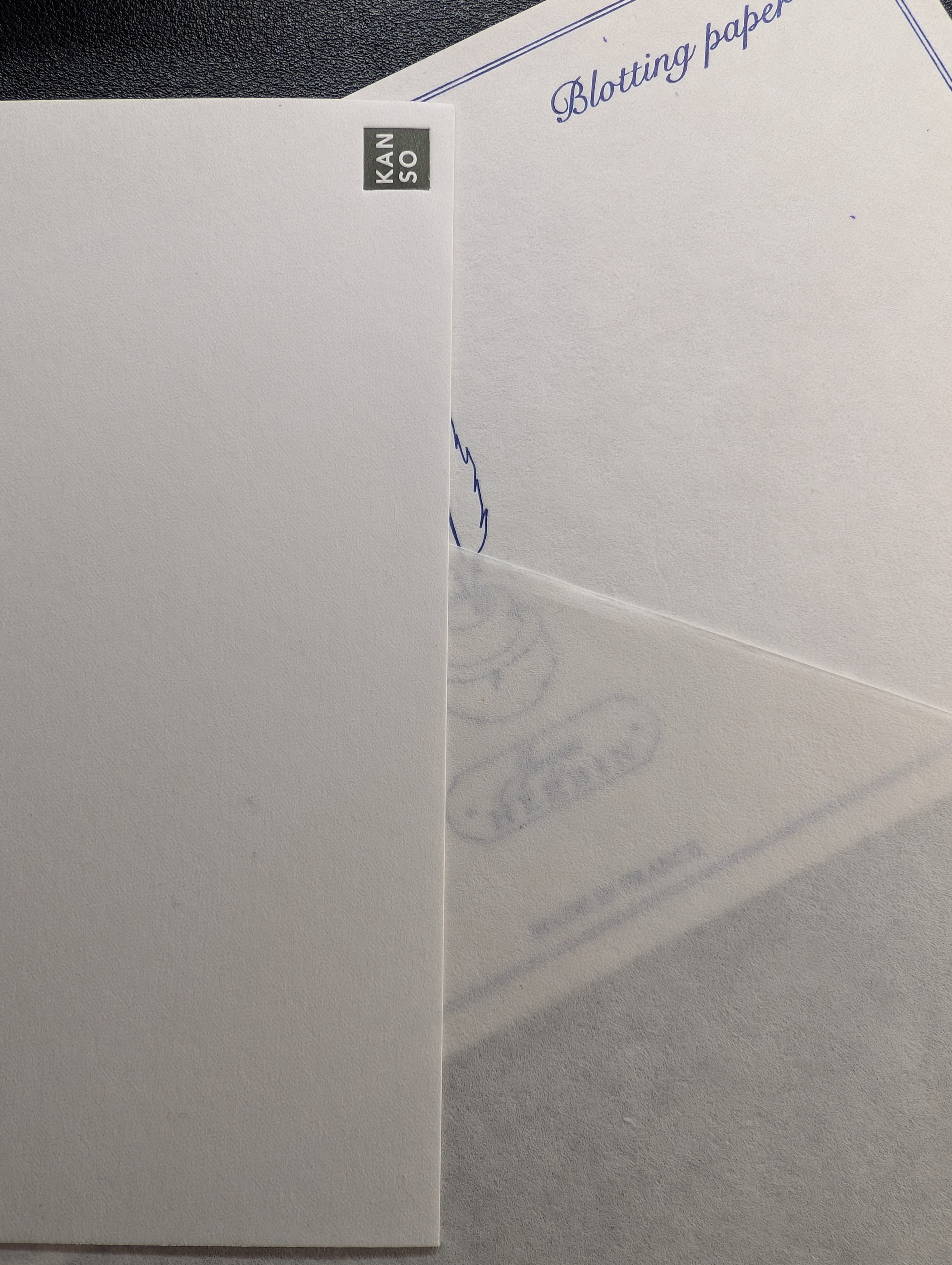 Photo of three overlapping sheets of blotting paper. The Herbin in the back has a pen and quill design and lettering. The Sakae paper at the bottom shows some of the Herbin design indicating how transparent it is. The Kanso paper on the left has a square "KANSO" logo in the corner and is thick enough that it's opaque.