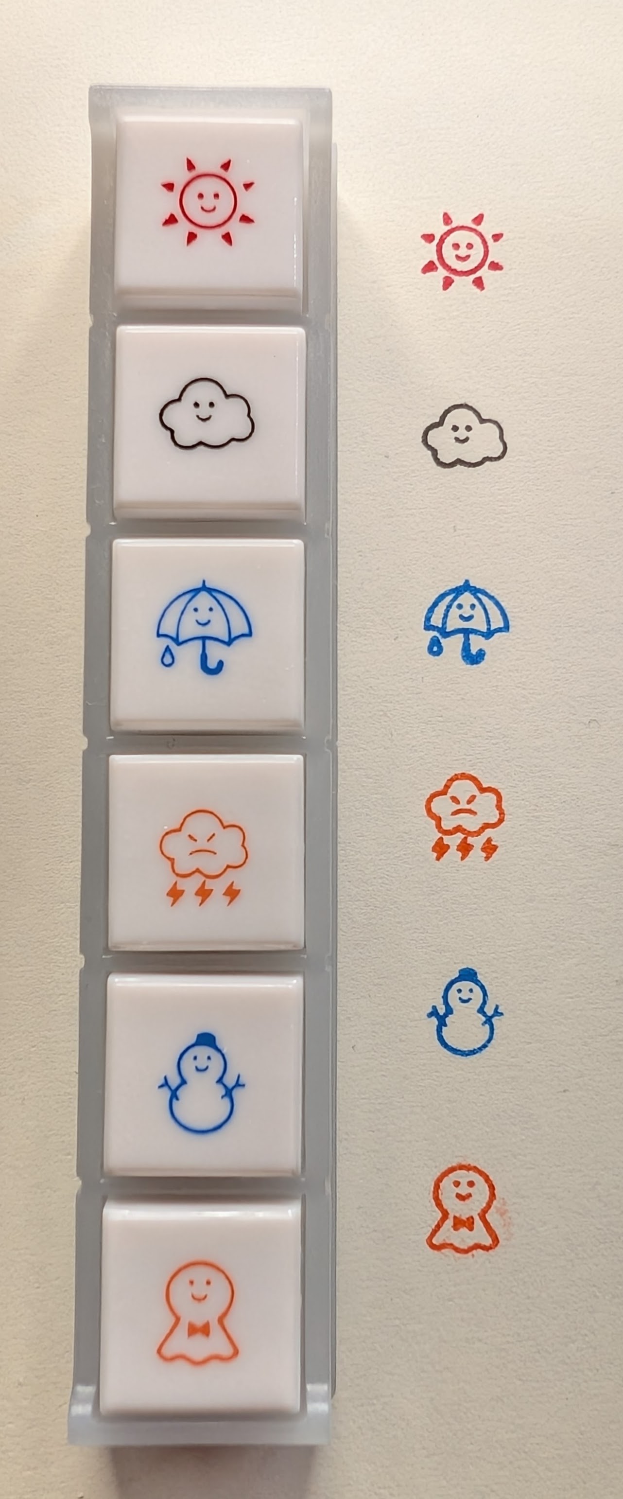 A row of six linked weather-related stamps next to their stamp marks on paper. The marks match the icon on the stamp. From top to bottom they are: - A smiling red sun - A smiling dark grey cloud - A smiling blue umbrella with a raindrop - An angry orange cloud with lightning - A smiling blue snowman - A smiling orange ghost with a bowtie shaped like a cloth wrapped around a ball.