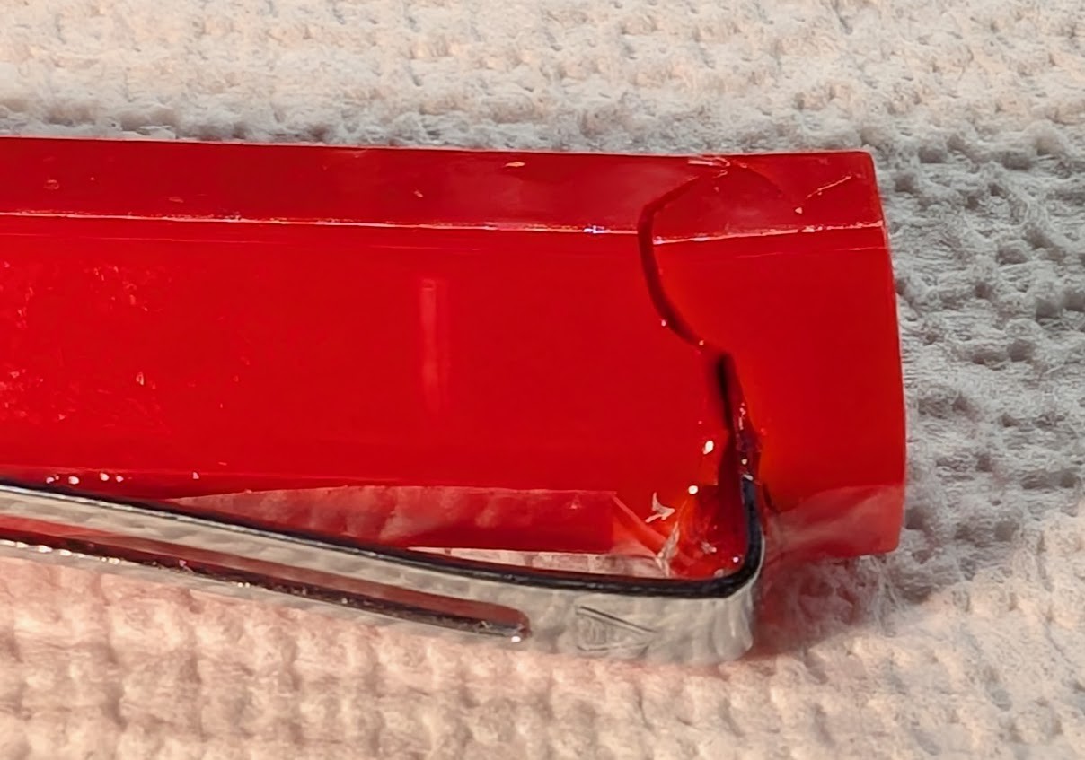 Photo of a red fountain pen cap with a silver clip. There are large jagged cracks starting at the hole where the clip enters the cap. The cracks extend all the way around the cap.