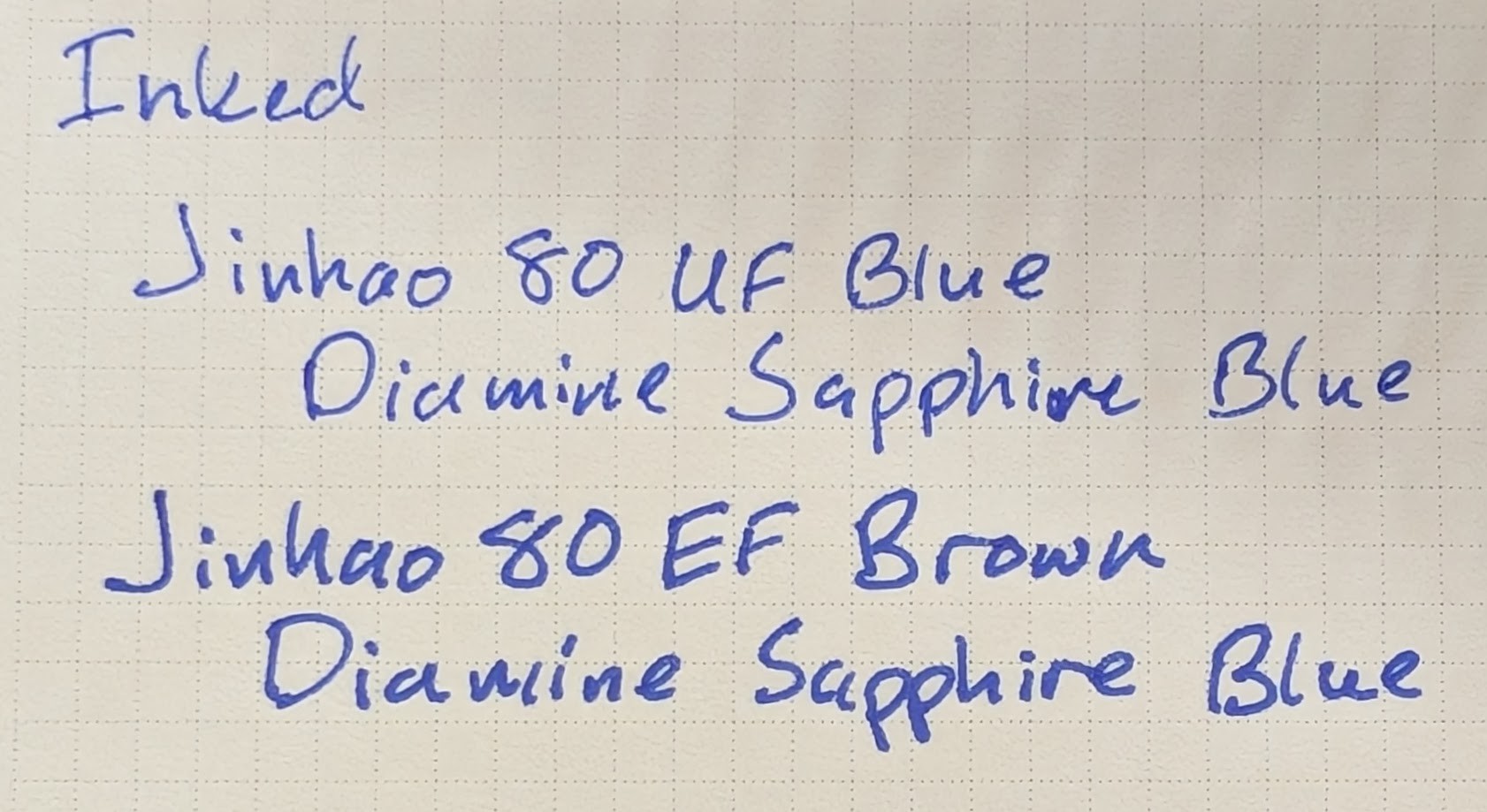 Photo of a writing sample on paper. The first lines read "Inked / Jinhao 80 UF Blue / Diamine Sapphire Blue" The last lines read "Jinhao 80 EF Brown / Diamine Sapphire Blue" -- this writing sample is a bit thicker than the top one, making the letters appear bold in comparison.