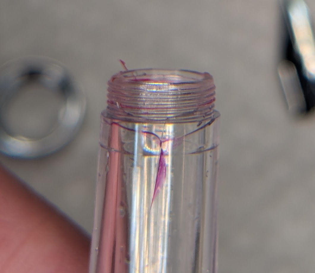 Close up photo of a cracked fountain pen section. There is a lengthwise crack along the section that splits into two "arms" which stretch out horizontally left and right