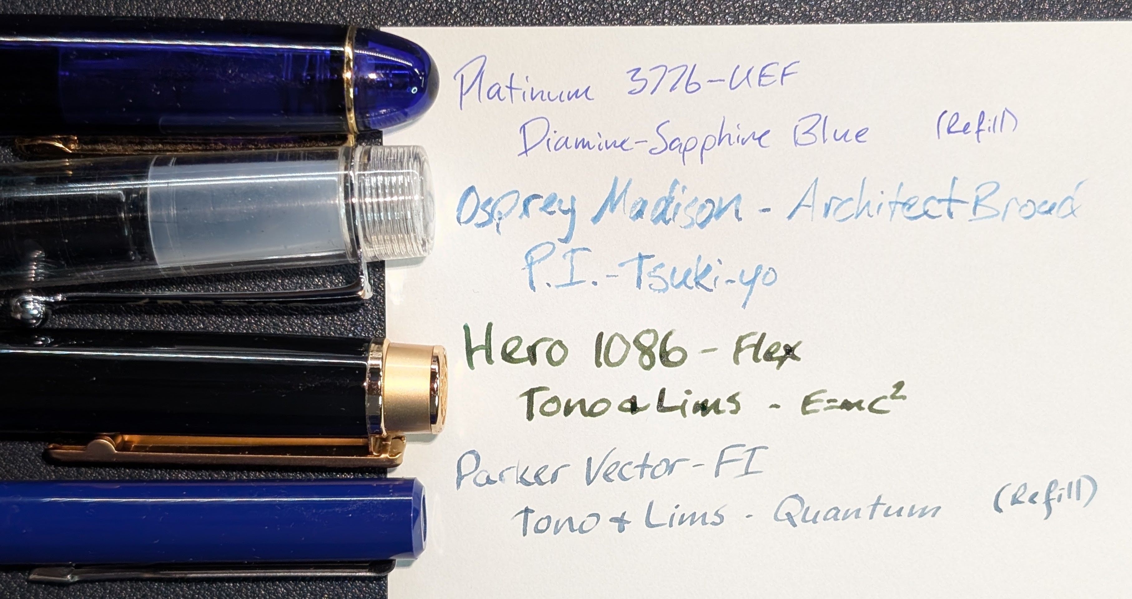 Photo of four fountain pens next to a paper with writing on it. Each pen corresponds to a writing sample on the paper, and the writing describes the pen and ink: - "Platinum 3776 - UEF / Diamine - Sapphire Blue (Refill)" - The pen is blue with gold trim, the ink is blurple. - "Osprey Madison - Architect Broad / P.I. Tsuki-yo" - The pen is clear with silver trim, the ink is blue-green. - "Hero 1086 - Flex / Tono & Lims - E=mc2" - The pen is black with gold accents, the ink is olive green. - "Parker Vector - FI / Tono & Lims - Quantum (Refill)" - The pen is blue with a silver clip, the ink is slate blue
