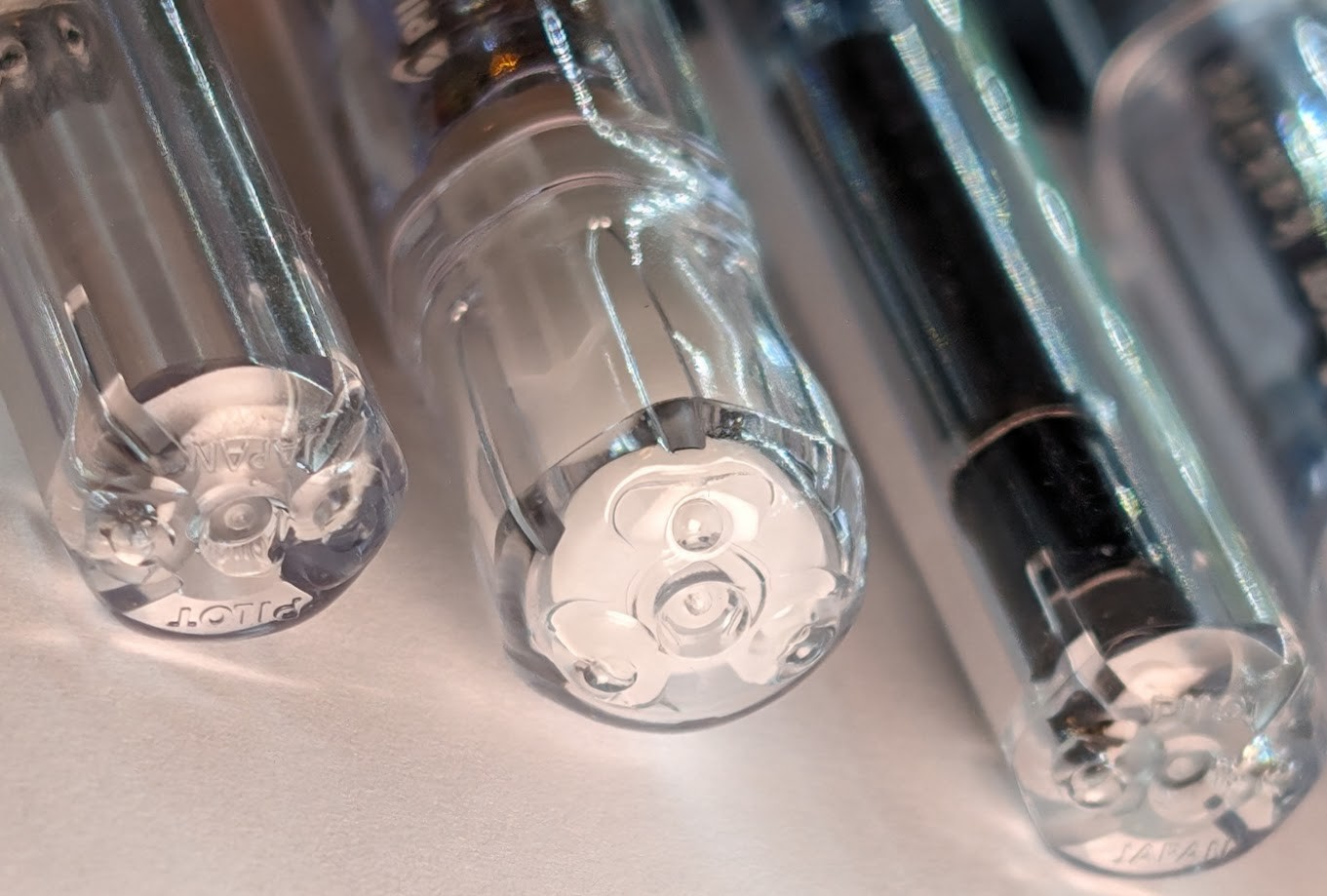 Photo of the ends of three fountain pens. Two have the rear end visible, one has the cap visible. Each of them have small ventilation safety holes which have been blocked with clear UV cure resin. Looking closer it's possible to see a little outline where the resin flowed.