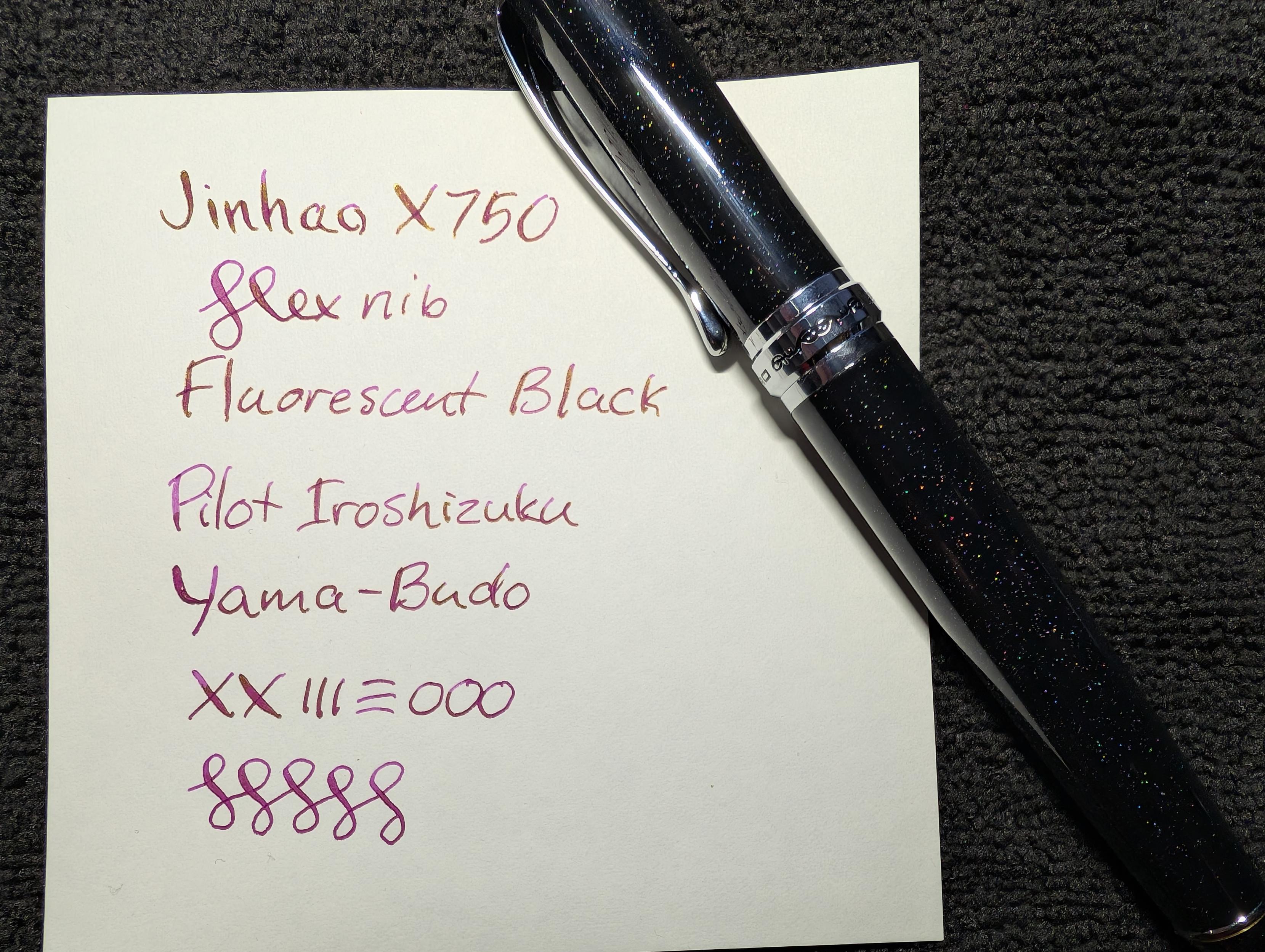 Fountain pen and writing sample. The pen is black with a little sparkle giving it a slight starry night sky look. The writing sample reads "Jinhao X750 / Flex Nib / Fluorescent Black / Pilot Iroshizuku / Yama-budo" followed by various lines and curlicues. The ink is dark fuchsia with gold sheen visible in several places.
