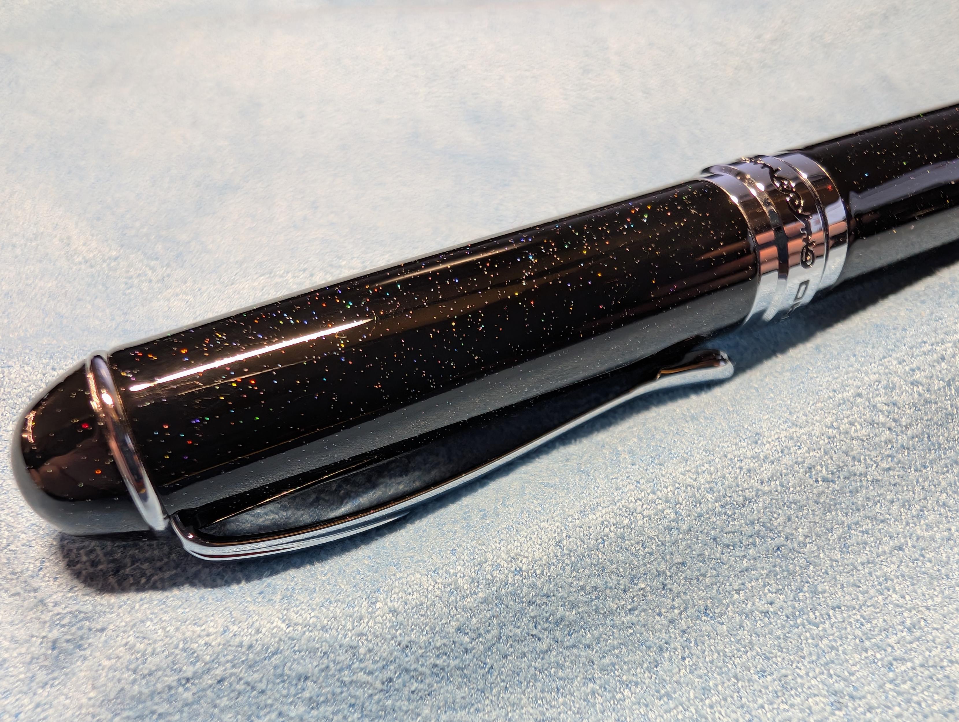 Close angle of the pen cap. The pen is black with a little sparkle giving it a slight starry night sky look. The trim is silver, and "Jinhao" can be read in the band around the center.