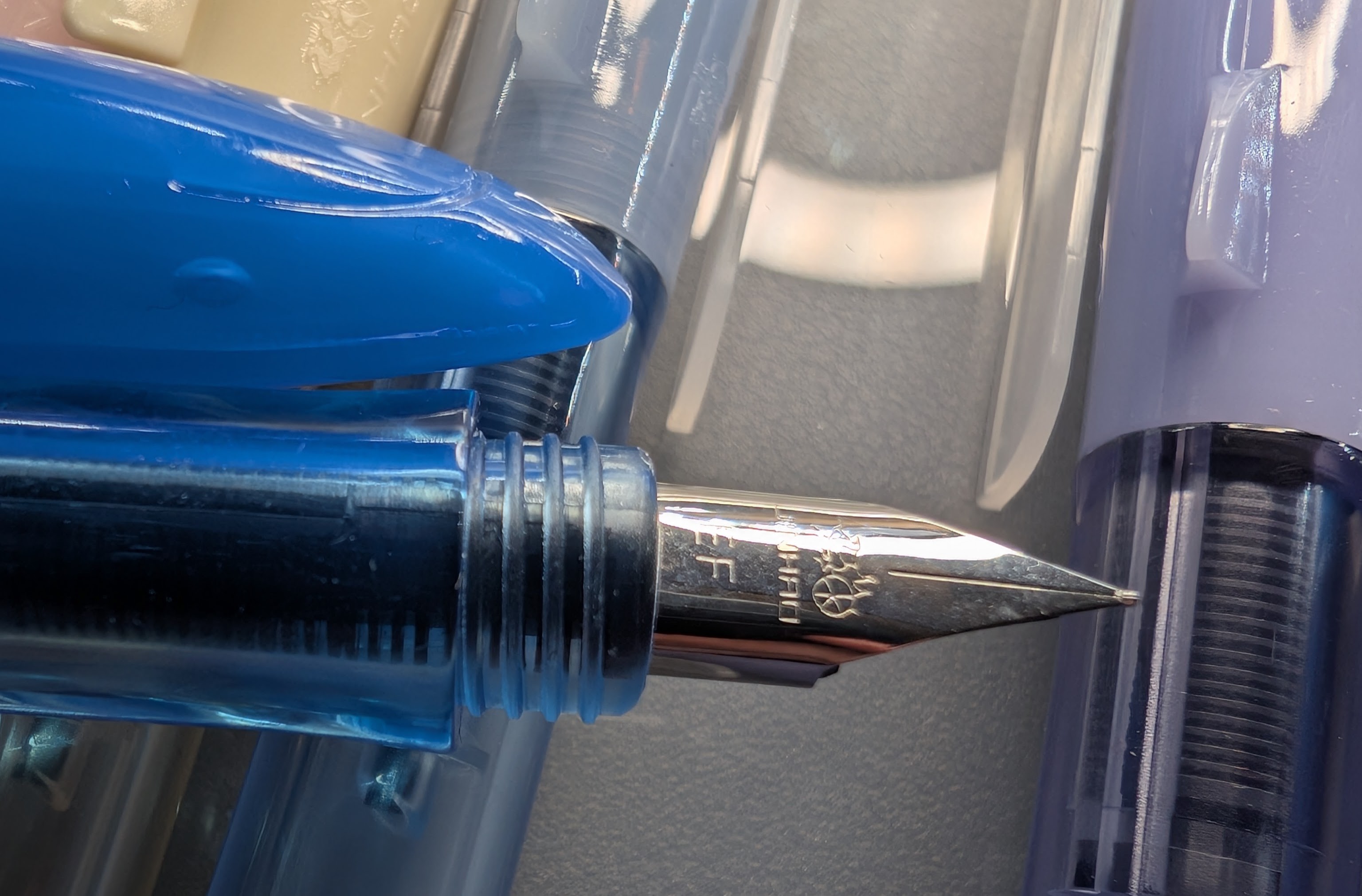 close-up photo of a fountain pen nib and the nose of its shark cap next to it. The nib is labeled "EF" with the Jinhao logo above the letters. It is an exposed nib and comes to a sharp point.