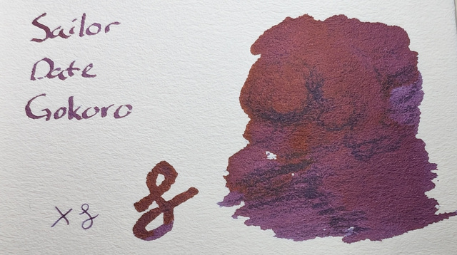 Swatch card reading "Sailor Date Gokoro", a couple pen scratches, and large blobs of ink made with the back end of a glass dip pen. On this paper the ink appears to be a dark red/purple with some reflective sheen overall.