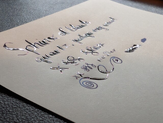 Photo of ink writing on paper taken at a low angle, the specific words are hard to make out, but there is a lot of wet ink collected on the lines reflecting light