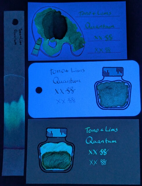 Same as the last photo but under primarily UV light.  The Iroful paper is glowing and the ink swatch is glowing green.  The col-o-ring paper is glowing very brightly and the ink in the bottle is glowing greenish, the cap is glowing light blue, and the text is glowing more blue.  The Midori paper is not glowing, and the ink is glowing teal/greenish in the text and top of bottle, the bottle cap is more blue, while the bottom of the bottle is glowing even more teal/green.  The chromatography strip has a greenish glow extending far past the end of where the blue was in the previous photo, and a slight halo of light blue going even farther than the green.